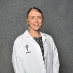 A woman in a white veterinarian's coat in front of a gray backdrop