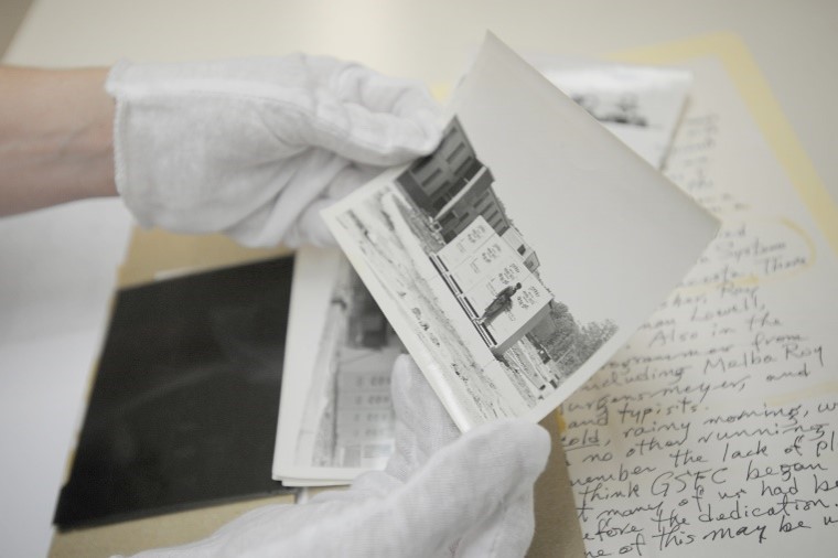 An archivist holds a photo from Goddard's early history in her gloved hands. Other archival documents from the collection appear in a folder in the background.