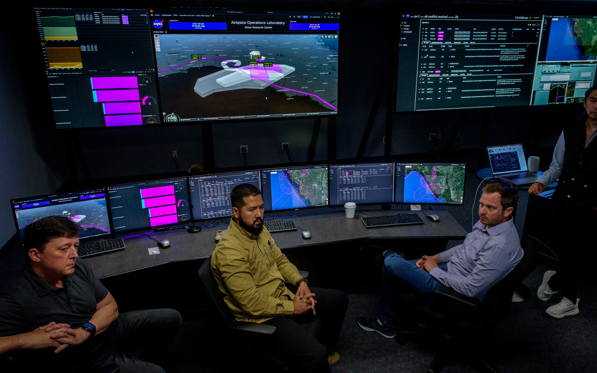 Three air traffic management specialists sit in font of a bank of computer screens.