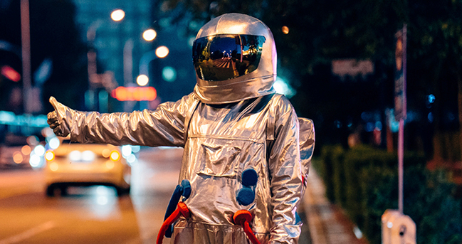 Mann in einem Astronautenanzug in Anhalterpose an einer Straße