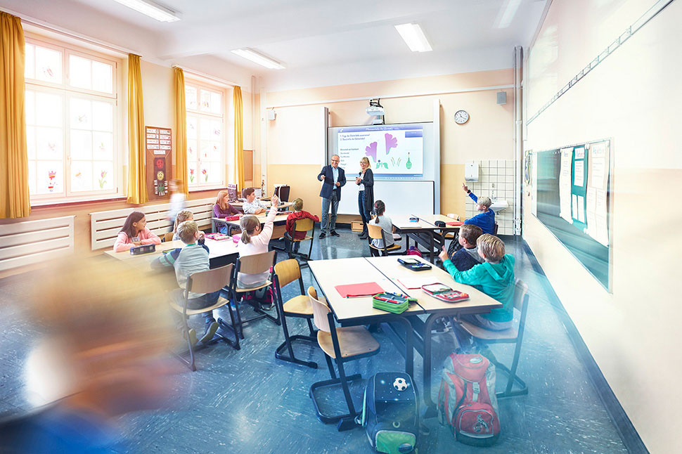 Unterrichtsraum einer Schule mit lernenden Schülern an drei Tischen.