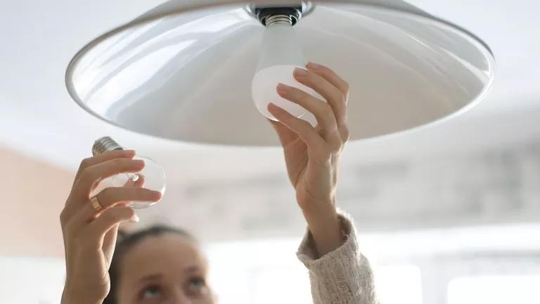 A person replaces an incandescent lightbulb with a new LED bulb.