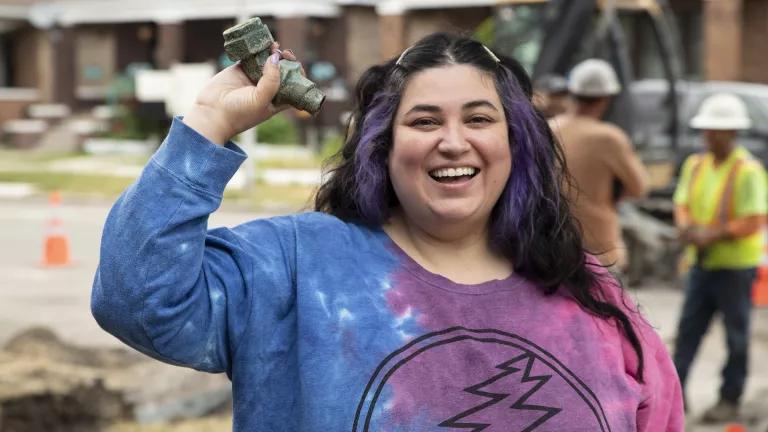 Gina Ramirez smiling as she holds up part of an old lead service line