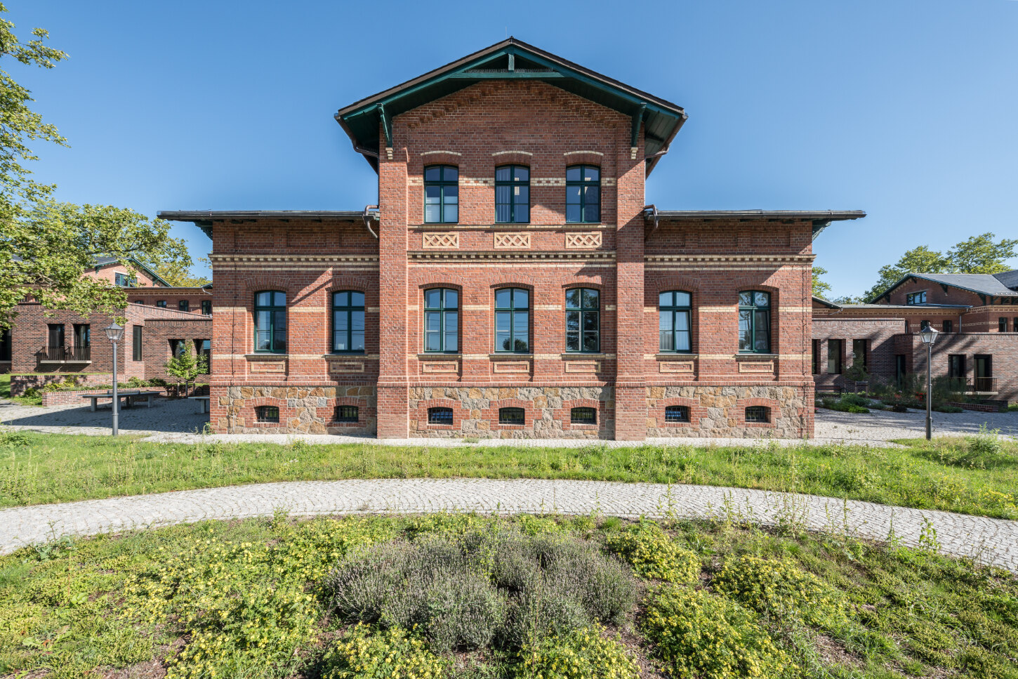 Die Fassade des Behandlungszentrum besteht weiterhin aus Ziegelsteinen und hat seine historische Musterung und Verzierung behalten. Die schwarzen Dachflächen stehen leicht über.