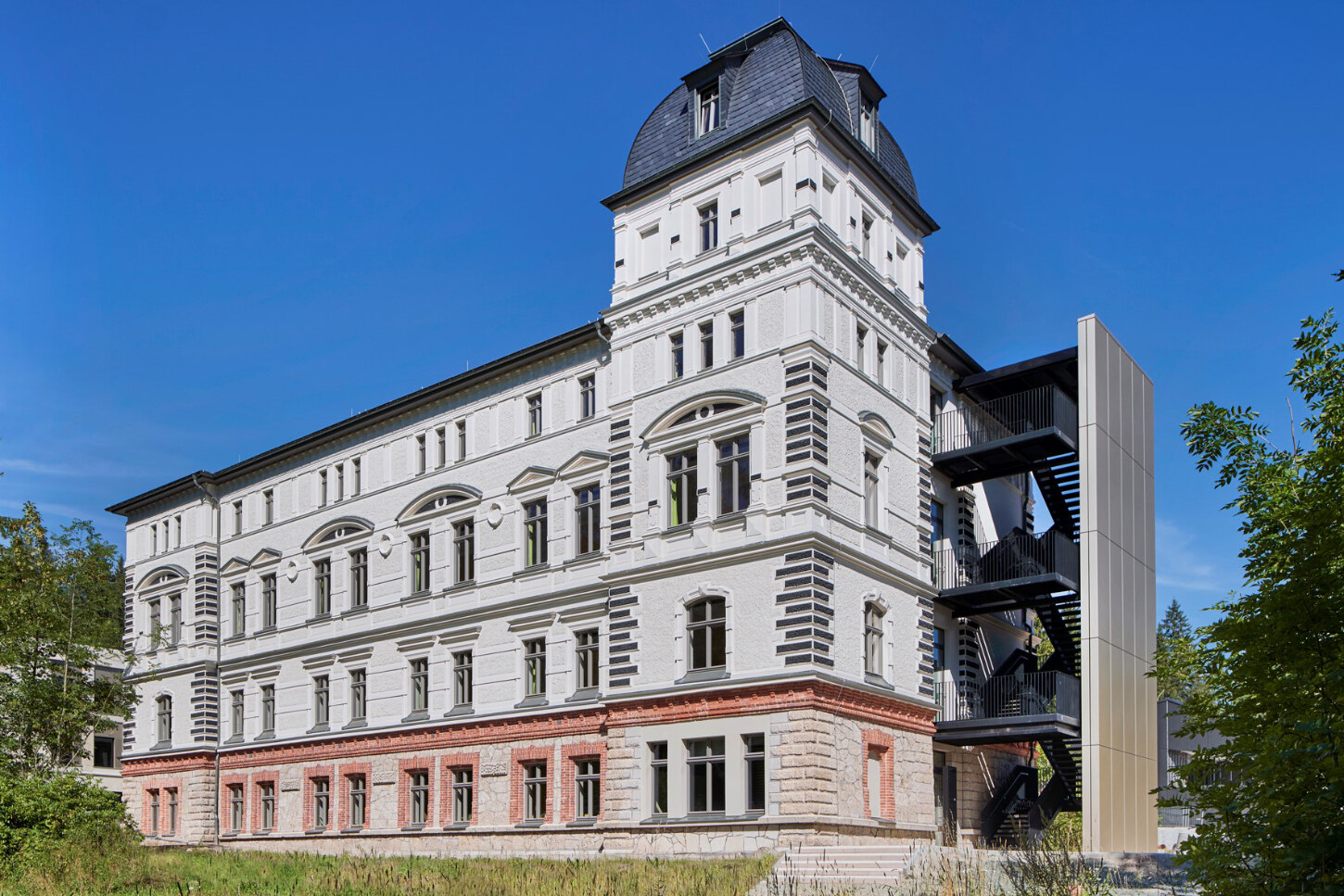 Das schwarze Dach und die weiße Fassade bilden einen guten Kontrast. Im unteren Bereich umranden rote Ziegelsteine die Fenster und markieren auch die erste Deckenhöhe.