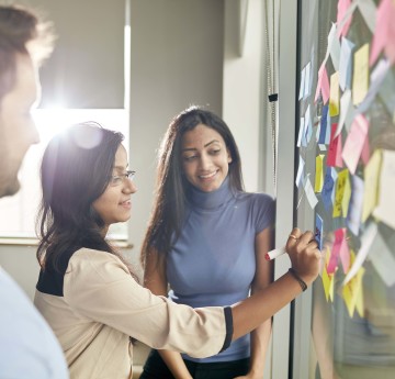 three members of staff project planning with post it notes on a wall. 