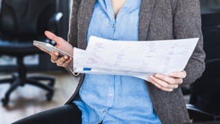 Frau im Büro hält Unterlagen und ein Smartphone in der Hand