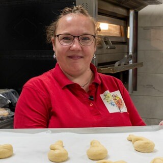 Junge Frau in Bäckerei mit Backblech in der Hand