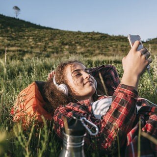 Eine junge Frau liegt im Gras und hört Podcast