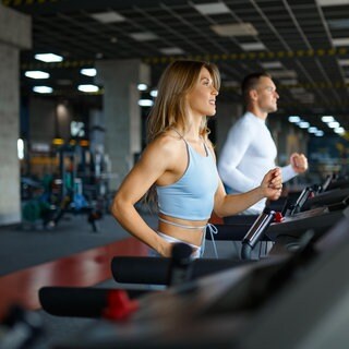 Eine Frau und ein Mann laufen auf Laufbändern im Fitnessstudio. 10.000 Schritte, Muskelkater ist gut, Joggen zum Abnehmen und gezielte Fettverbrennung: Sportwissenschaftlerin Dr. Mona Kellner klärt Mythen zu Sport und Ernährung auf.