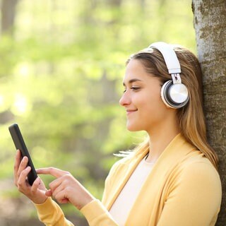 Junge Frau hört Musik über ihr Smartphone und hat Kopfhörer auf.