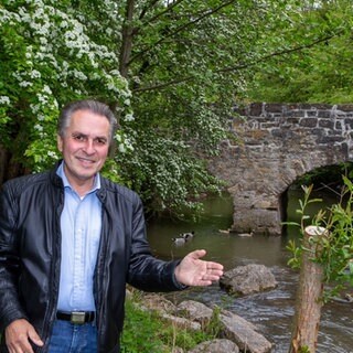 Naturschützer Claus-Peter Hutter zeigt mit der Hand auf einem Bach mit einer Steinbrücke.