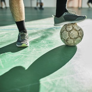 Ein Mann stoppt mit seinem Fuß einen Fußball in einer Sporthalle.