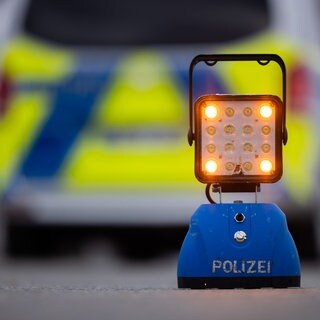 Ein Warnlicht mit der Aufschrift "Polizei" steht auf der Straße vor einem Einsatzfahrzeug der Polizei (Symbolbild).