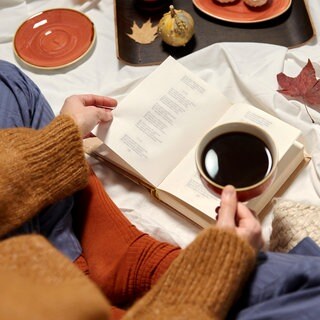 Person mit Tasse und Buch in der Hand, herbstlich geschmückt