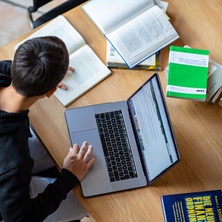 Student arbeitet an einer Hausarbeit mit Laptop und Büchern, tags: KI, ChatGPT, Uni