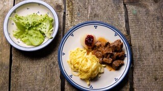 Lammgulasch mit Tagliatelle und Blattsalat auf einem Teller