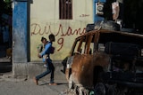 Seventeen-year-old Sevenson carries his 3-year-old little sister to school past the burned out remains of a car in a street of the Canape Vert neighborhood of Port-au-Prince, Haiti