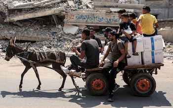 Men ride a donkey-drawn cart carrying aid boxes provided by the United Nations Relief and Works Agency for Palestine Refugees (UNRWA), as it moves past a collapsed building with a concrete block bearing graffiti reading in Arabic "to passersby over our dreams, this is Gaza", along a street in central Gaza City