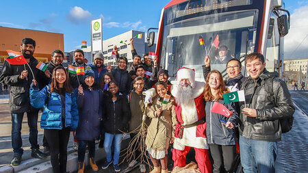 Ein Weihnachstmann und viele junge Leuten stehen vor einer Straßenbahn.