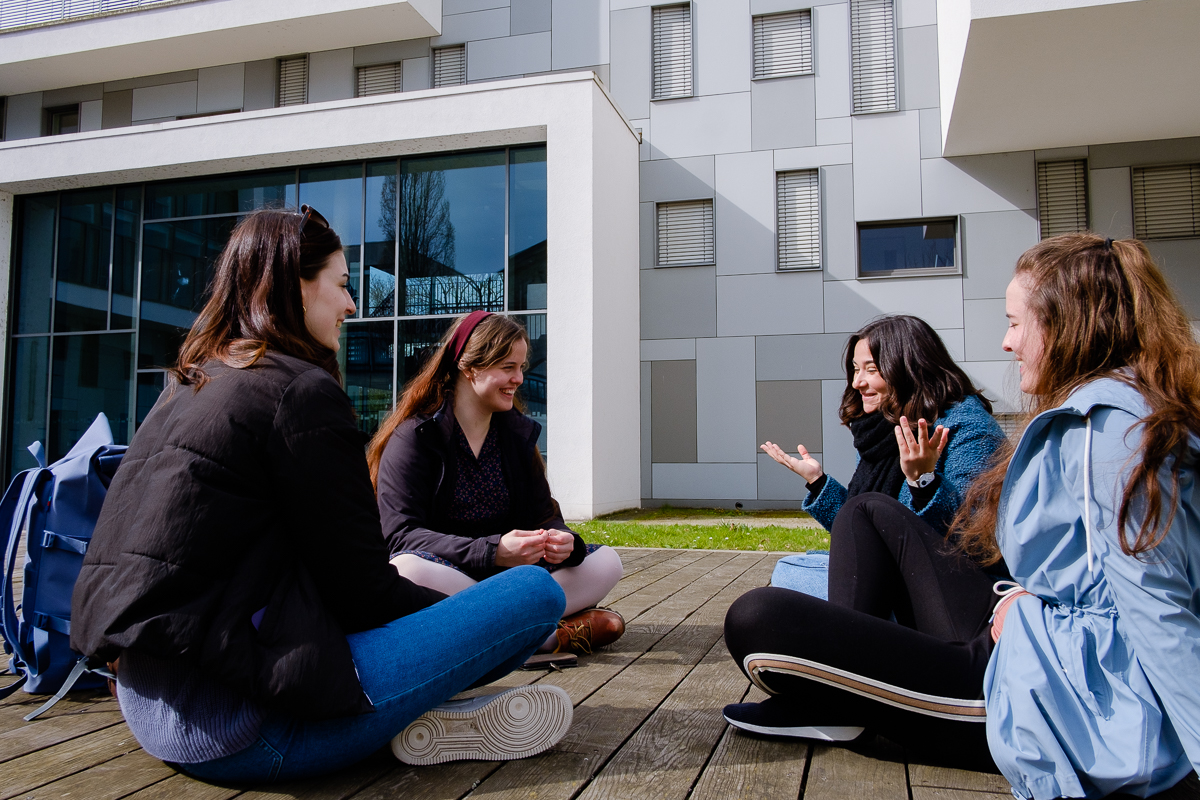 Studentinnen sitzen auf einer Wiese und unterhalten sich.