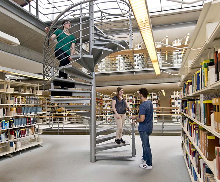 Three students standing at a spiral staircase in a library