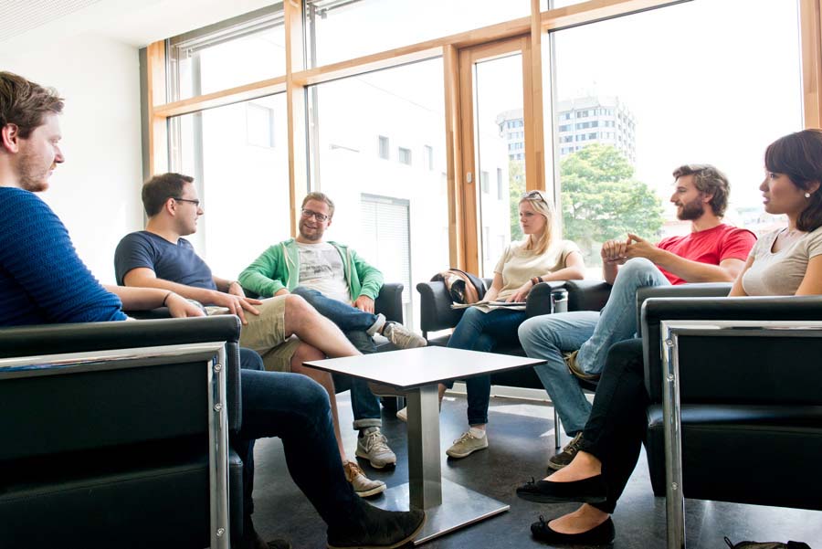 Eine Gruppe von sechs Studierenden, vier Männer und zwei Frauen, sitzen in einem Stuhlkreis und diskutieren angeregt.