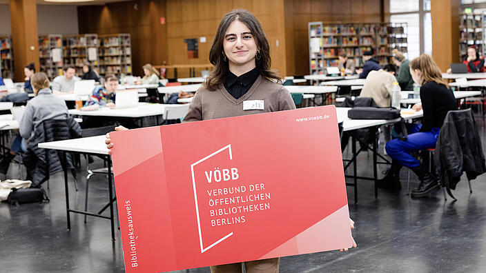 Junge Frau mit sehr großem Bibliotheksausweis in der Lesehalle der BStB