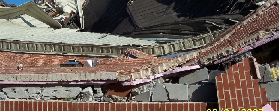 Brick wall that has been curved upwards where the metal roof was peeled back.