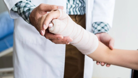 Eine Person im Kittel hält einen Arm, der einen Gips trägt