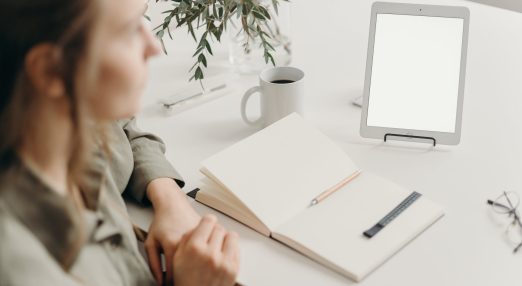 Person in gray jacket sitting beside table with white printer paper and white ceramic mug