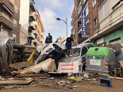 Tres jóvenes saltan a través de un muro de coches que ha formado la riada en Alfafar (Valencia), este miércoles.