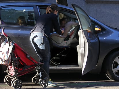 Una mujer saca del cochecito a su hijo y lo coloca en una silla portabebés, en el asiento delantero de un coche.