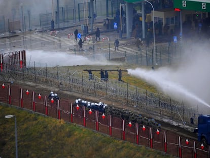 Las fuerzas polacas actúan con cañones de agua contra cuatro migrantes que corren con un tronco hacia la valla, este martes en el puesto fronterizo de Bruzgi-Kuznic.