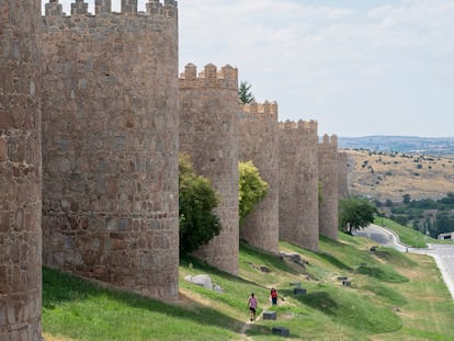 Dos paseantes siguen la muralla de Ávila extramuros.