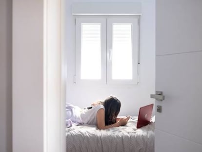 Una joven consulta el móvil y el ordenador en su habitación.