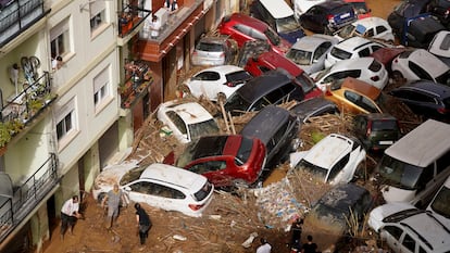 Residents clean the street next to cars piled up after being swept away by floods in Valencia, Spain, Wednesday, Oct. 30, 2024. (AP Photo/Alberto Saiz)