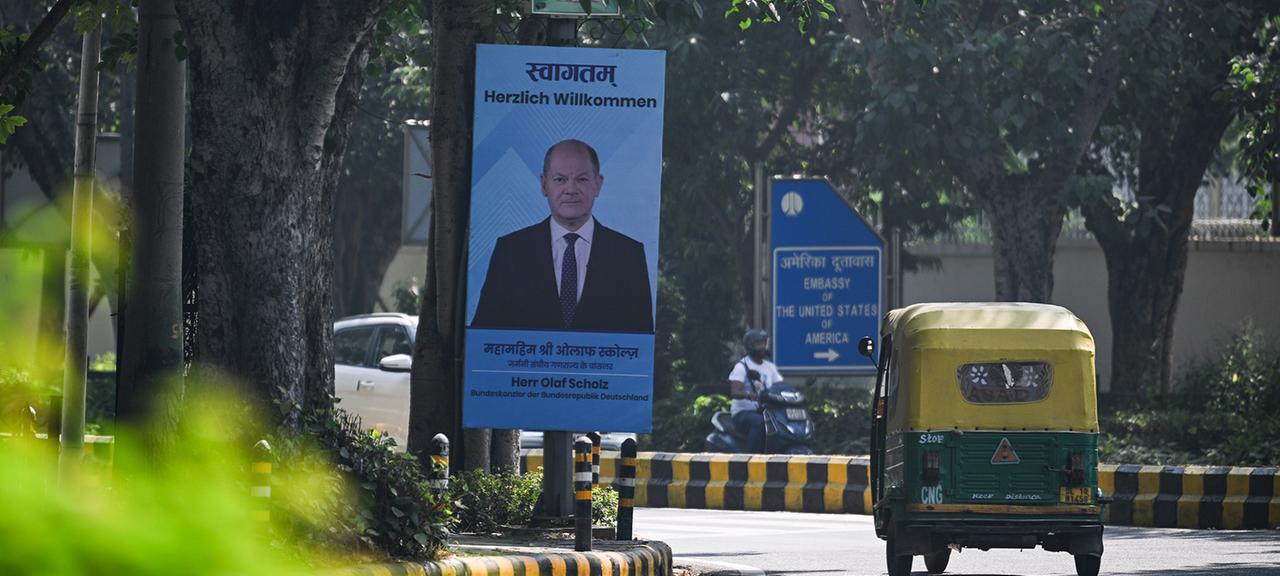 Ein Schild mit dem Bild von Olaf Scholz sowie dem Satz "Herzlich Willkommen" steht an einer Straße.