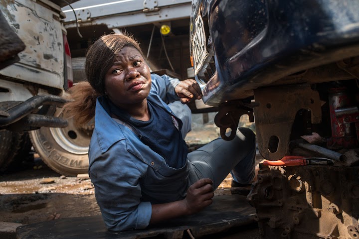 Princesse à l'œuvre sous une voiture dans une combinaison de travail bleue.