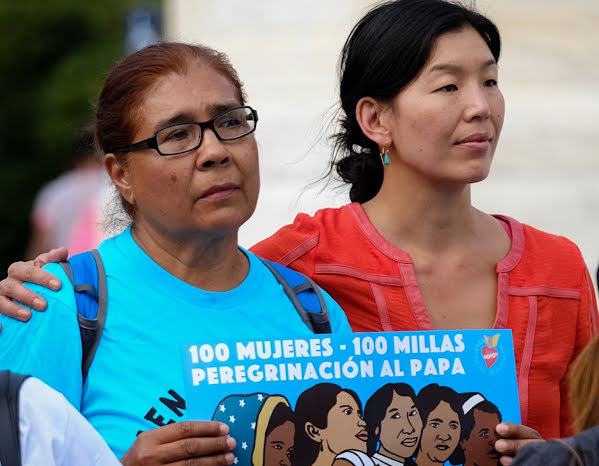 Women standing together in support and holding signs.