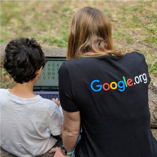 A Google.org fellow sits with a child, both focused on a laptop displaying the alphabet and numbers 1 through 10.