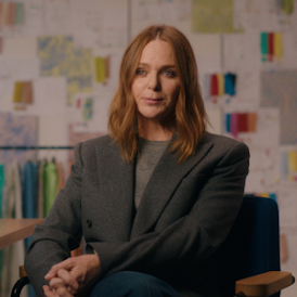 Un portrait de la créatrice de mode Stella McCartney dans son studio. Plusieurs tenues sont rangées derrière elle.