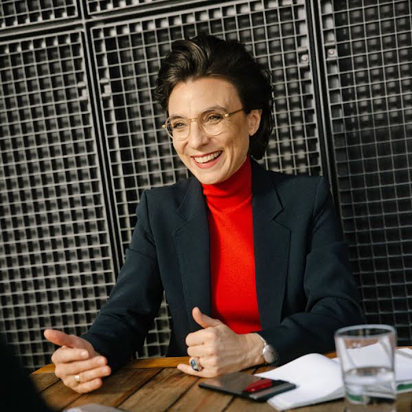 Christine Antlanger-Winter, Country Director von Google Schweiz, sitzt in einem schwarzen Blazer und rotem Rollkragenpullover an einem Holztisch und redet mit einem nicht sichtbaren Gegenüber.