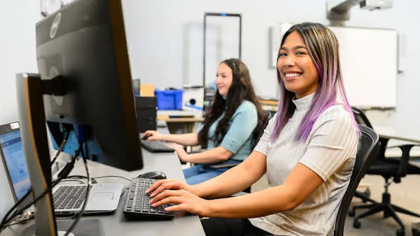 Two women working on their computers, one looking at the camera and smiling