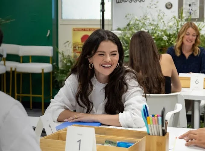 Selena Gomez sits with young teenagers at a table filled with art supplies.