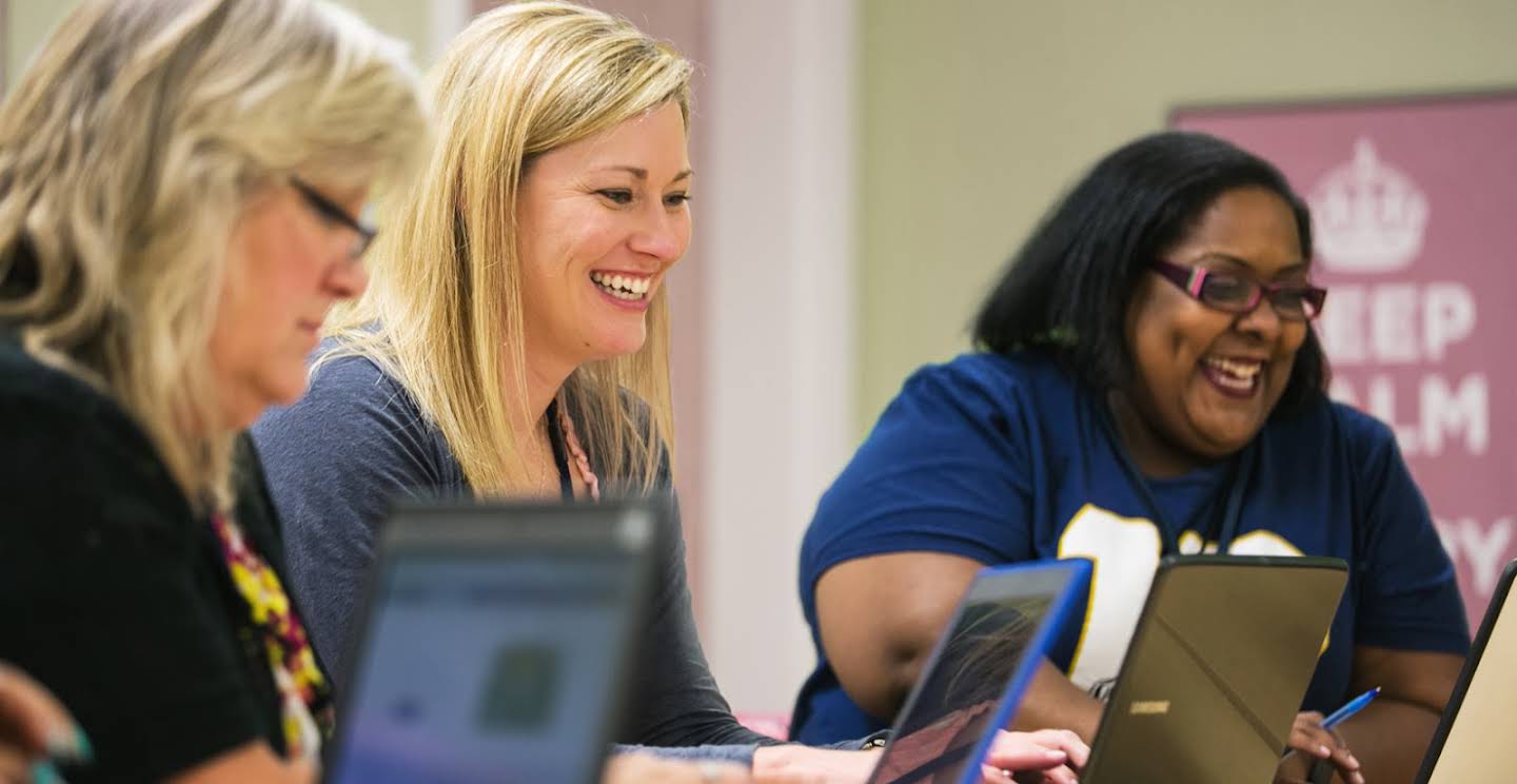 Drie docentes glimlachen terwijl ze aan hun laptop zitten.