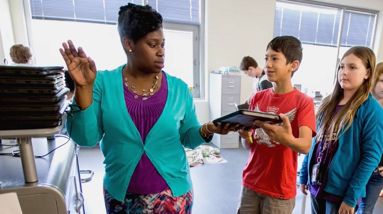 Femme distribuant des Chromebooks aux élèves d'une classe.