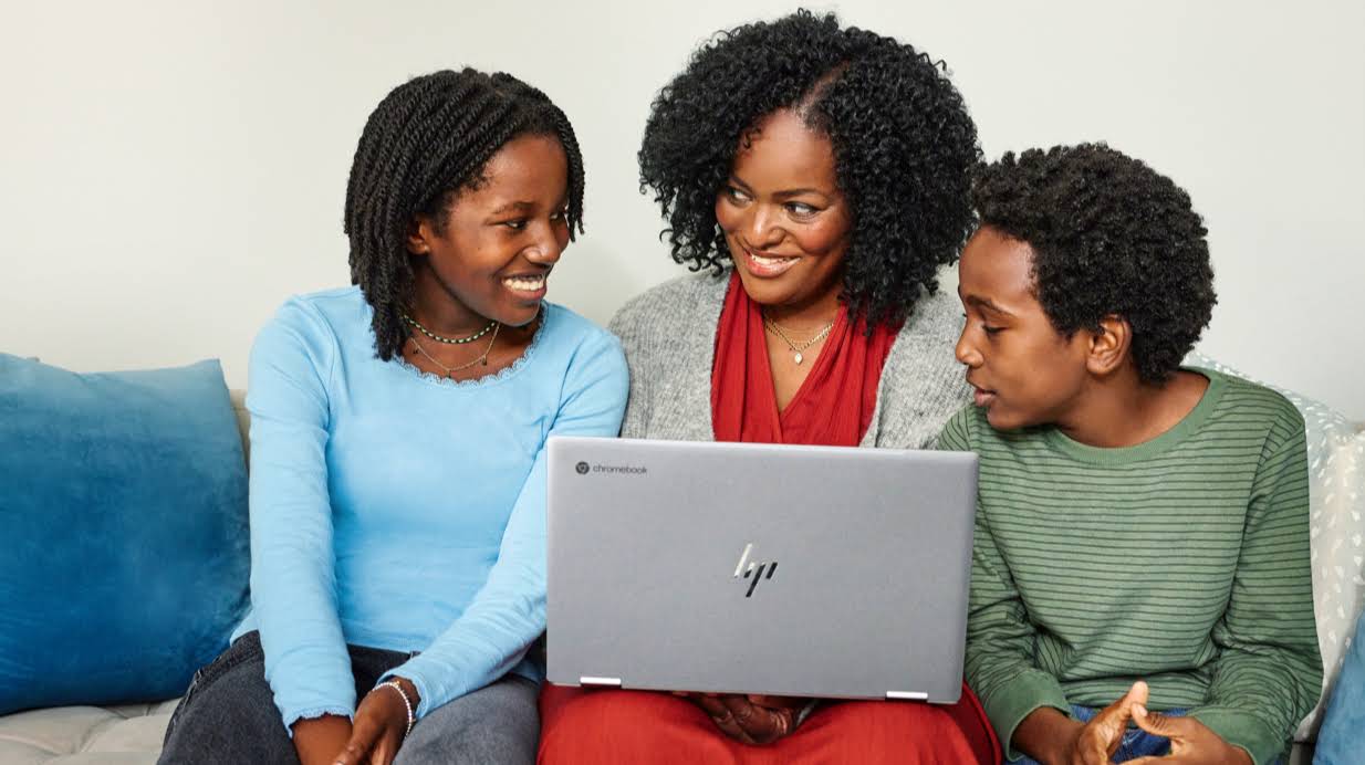 Une mère de famille entourée de deux enfants sur un canapé et tapant sur le clavier d'un Chromebook.