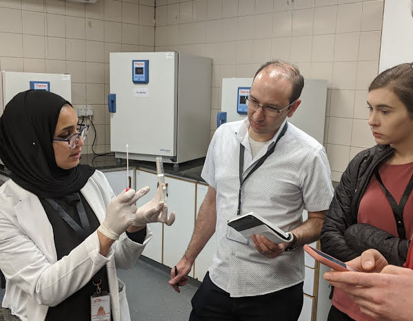 A group of people in a medical lab listening to one talk about testing.