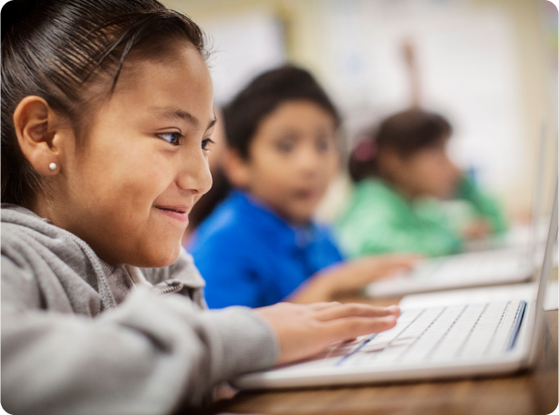 A student smiles while working on a Chromebook in class.